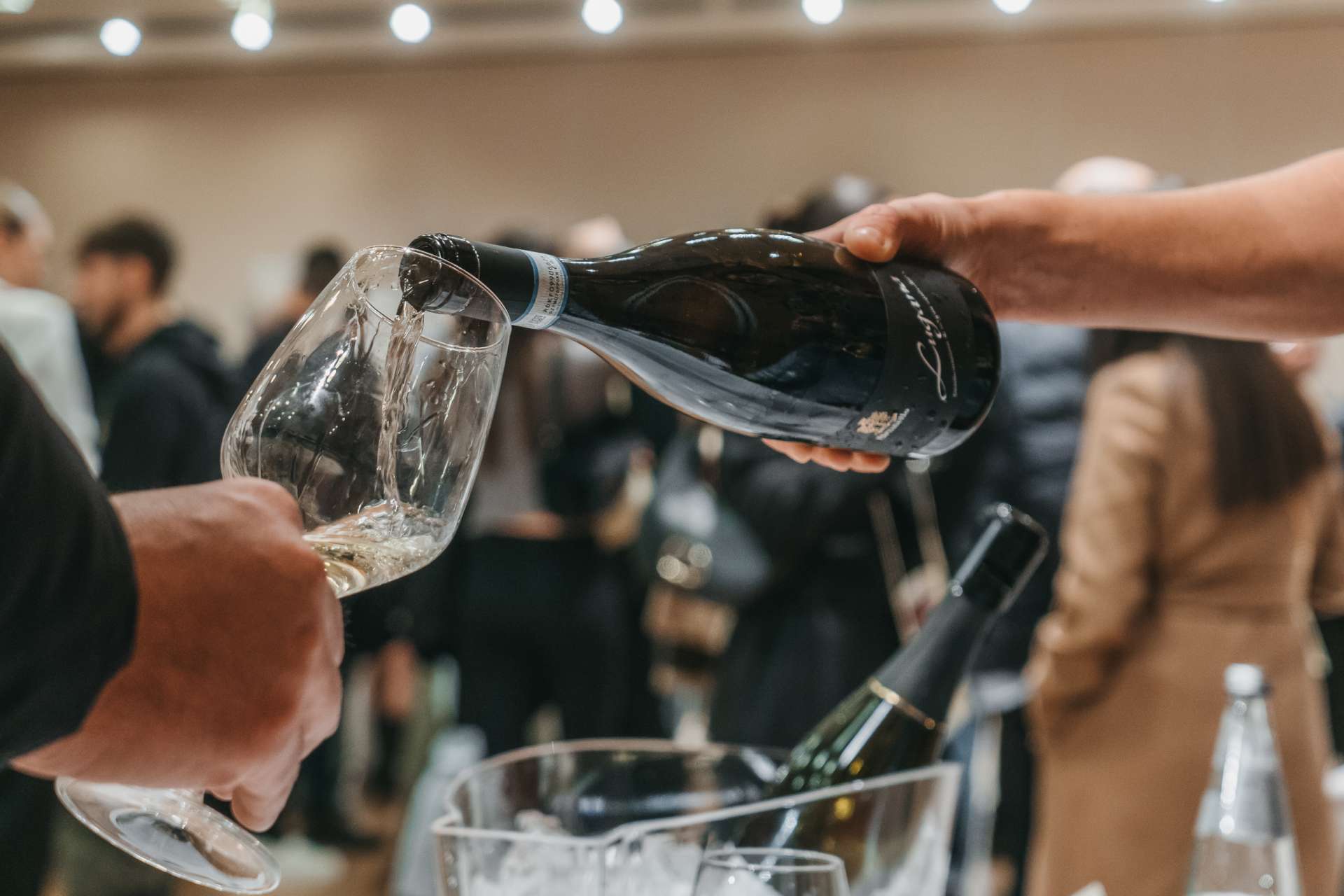 Dettaglio di una bottiglia di vino bianco spumante che viene servito su calice, all'evento Degustando di PD Distribuzione